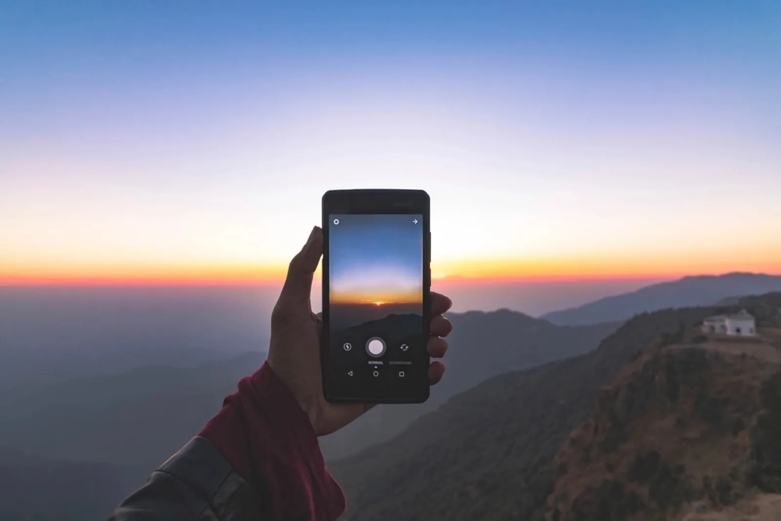 Hand holding a phone upright, filming a sunset