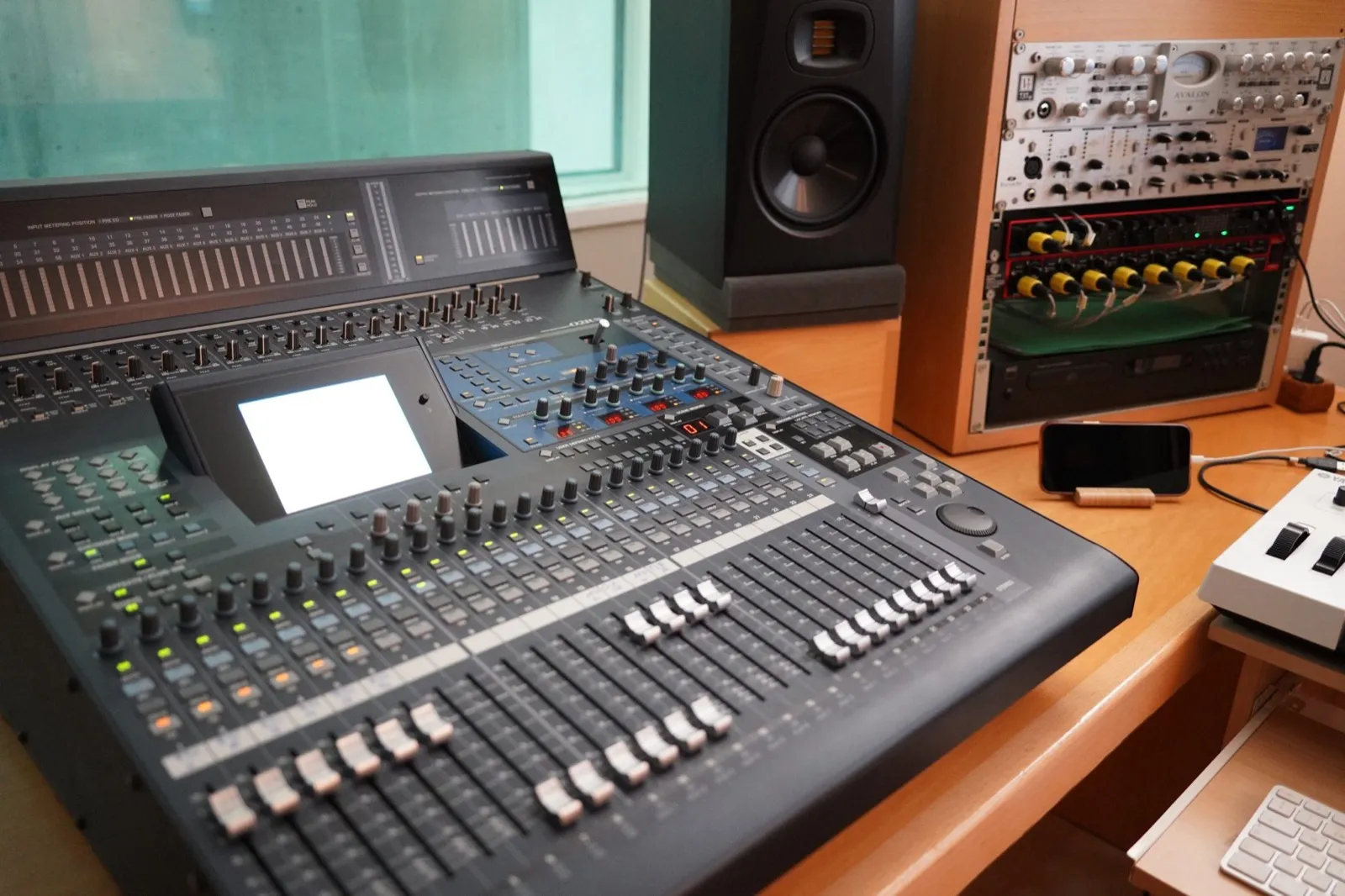 A digital mixing console with rows of faders in a small studio