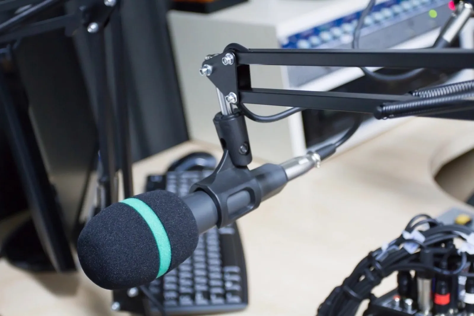 A broadcast microphone on a boom arm over a desk with a keyboard and mixer